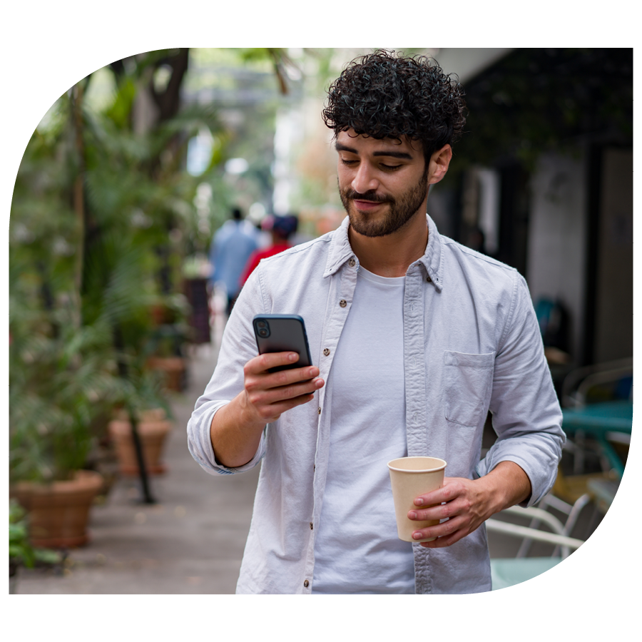 young man checking smartphone walking with coffee through city