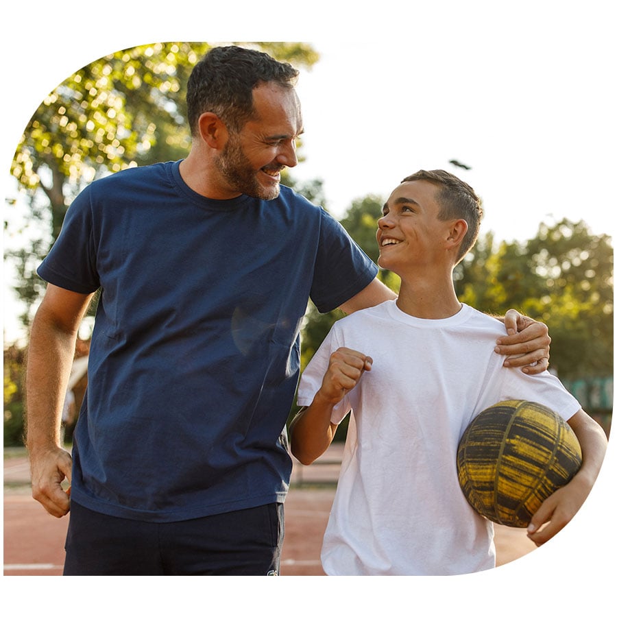 A father and son in the park smiling after playing basketball