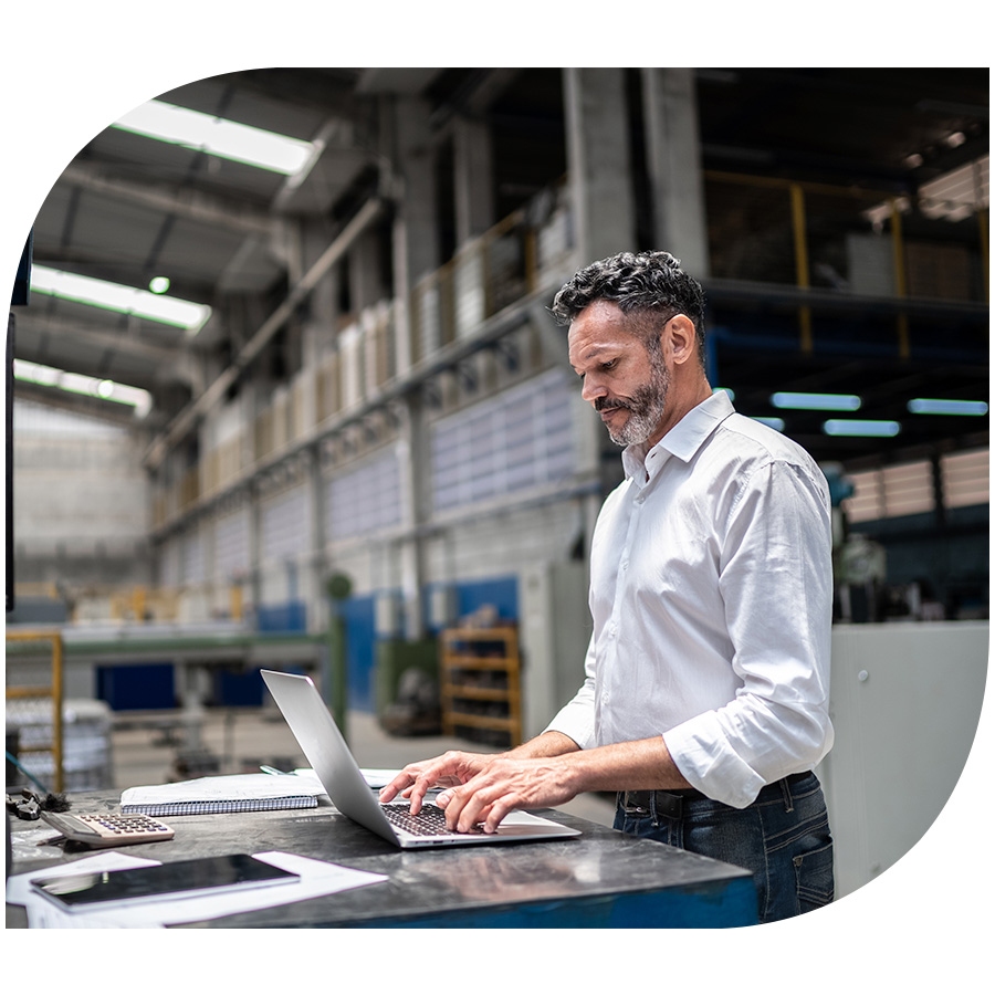 A man in a collared shirt working on a laptop in an industrial building