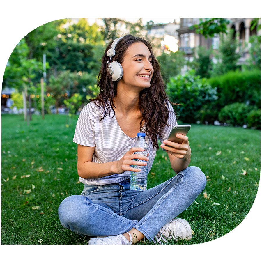 A young woman wearing headphones sitting in the park smiling and listening to music