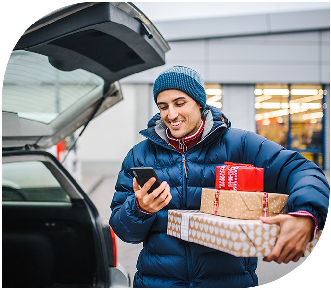 man smiling at his phone while loading holiday gifts in his car